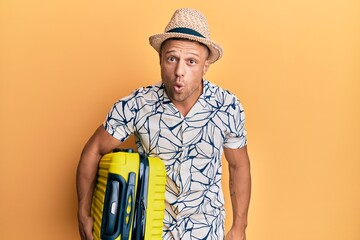 Poster - Handsome muscle man holding suitcase going on summer vacation scared and amazed with open mouth for surprise, disbelief face