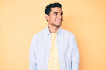 Canvas Print - Young handsome hispanic man standing over yellow background looking to side, relax profile pose with natural face and confident smile.