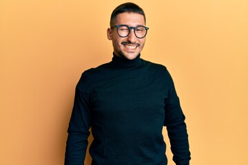 Poster - Handsome man with tattoos wearing turtleneck sweater and glasses winking looking at the camera with sexy expression, cheerful and happy face.