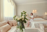 Fototapeta Koty - A girl in a white negligee is sitting on the bed with a bouquet of white roses in her hand