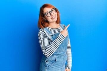 Wall Mural - Beautiful redhead woman wearing casual clothes and glasses smiling cheerful pointing with hand and finger up to the side