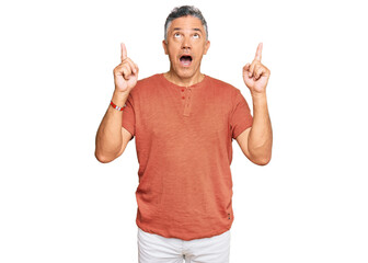 Canvas Print - Handsome middle age man wearing casual clothes amazed and surprised looking up and pointing with fingers and raised arms.