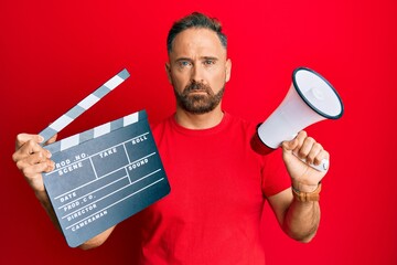 Sticker - Handsome middle age man holding video film clapboard and megaphone depressed and worry for distress, crying angry and afraid. sad expression.