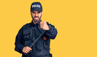 Canvas Print - Young hispanic man wearing police uniform holding baton annoyed and frustrated shouting with anger, yelling crazy with anger and hand raised