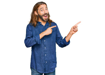 Attractive man with long hair and beard wearing casual clothes smiling and looking at the camera pointing with two hands and fingers to the side.