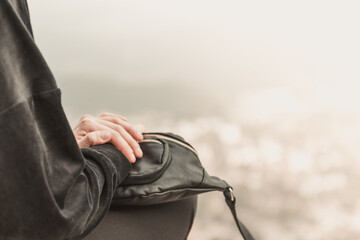 Primo piano di una donna che viaggia in possesso di una borsa in pelle si trova sul bordo di una scogliera tra le montagne.