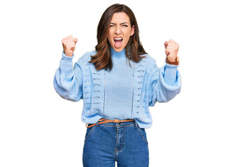 Canvas Print - Young brunette woman wearing casual winter sweater angry and mad raising fists frustrated and furious while shouting with anger. rage and aggressive concept.