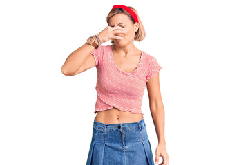 Sticker - Young blonde woman wearing casual clothes and diadem smelling something stinky and disgusting, intolerable smell, holding breath with fingers on nose. bad smell