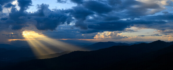 Wall Mural - the bright rays of the sun are shining from saturated clouds to mountain range before sunset.