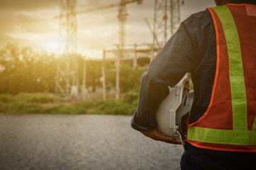 white helmet in the hands of an engineer with a sunset on the building construction background