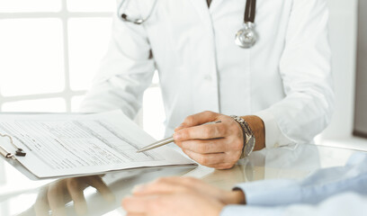 Unknown male doctor and woman-patient discussing current health examination while sitting in clinic and using clipboard. Good medical service in hospital. Medicine concept