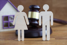 Wooden Figures Of Man And Woman Standing On Table Near Judges Hammer And Toy House Closeup. Divorce Mediation Concept