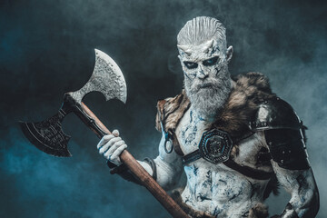 Armed with two handed axe northern dead warrior with naked torso and pale skin poses in dark smokey background.