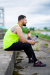 © Georgii - Cool young athletic guy with bottle of water sitting on stairs after training in urban in rainy weather