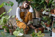 Tired woman gardener in glasses wear overalls takes a break from work, sitting, pruning dry withered caladium houseplant, take routine care, using scissors. Hobby, home gardening, indoor garden. 