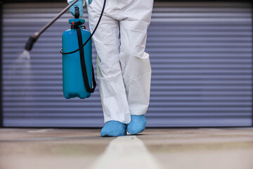 Wall Mural - Closeup of man in protective uniform with rubber gloves holding sprayer with disinfectant and spraying garage in order to prevent spreading corona virus.