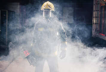 Wall Mural - Portrait of young fireman standing and holding a chainsaw in the middle of the chainsaw's smoke  .