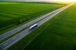 Leinwandbild Motiv blue truck driving on asphalt road along the green fields. seen from the air. Aerial view landscape. drone photography.  cargo delivery
