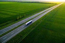 Blue Truck Driving On Asphalt Road Along The Green Fields. Seen From The Air. Aerial View Landscape. Drone Photography.  Cargo Delivery