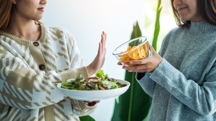 Wall Mural - Women choosing to eat vegetables salad and making hand sign to refuse potato chips