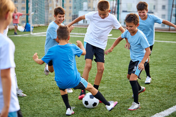 young caucasian school kids playing football in a field, stadium. boys 8-9 years old kicking soccer on the sports grass pitch, wearing sportswear on football match