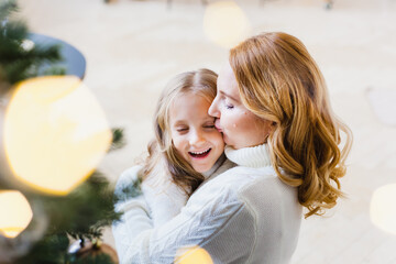 Wall Mural - A girl with her mother near the Christmas tree, the interior decorated for the new year and Christmas, family and joy, traditions