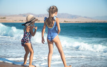 Two Little Girls Play Along The Beach By The Sea.