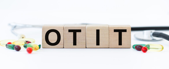 Wall Mural - cubes with the word OTIT on them. Care concept. Wooden cubes on a white background, next to scattered pills and a stethoscope