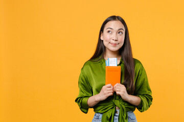 Wall Mural - Pensive pretty young traveler tourist asian woman in green shirt hold passport tickets looking up isolated on yellow background. Passenger traveling on weekends getaway. Air flight journey concept.