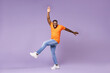 © ViDi Studio - Full length of cheerful funny young african american man 20s wearing basic casual orange t-shirt dancing rising leg spreading hands looking camera isolated on pastel violet background studio portrait.