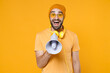 © ViDi Studio - Excited surprised shocked young bearded man 20s wearing basic casual t-shirt headphones eyeglasses hat standing screaming in megaphone looking camera isolated on yellow background, studio portrait.