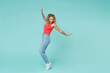 © ViDi Studio - Full length side view of excited cheerful young blonde woman 20s in pink tank top jeans standing on toes dancing spreading hands looking down isolated on blue turquoise background, studio portrait.