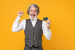 © ViDi Studio - Joyful elderly gray-haired business man in checkered waistcoat white shirt hold credit bank card doing winner gesture isolated on yellow background studio portrait. Achievement career wealth concept.