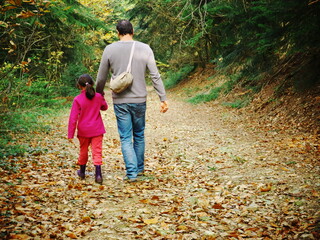 Photo of a father and daughter seen from behind, taking a walk in the forest holding hands