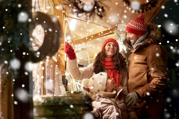 Wall Mural - family, winter holidays and celebration concept - happy mother, father and little daughter at christmas market on town hall square in tallinn, estonia over snow