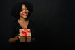 © etonastenka - A dark-skinned woman with an afro hairstyle gives a gift to the camera. The concept of New Year's shopping, gifts. Copy space