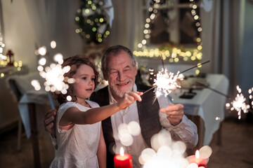 Poster - Senior grandfather with small granddaughter indoors at Christmas, having fun with sparklers.