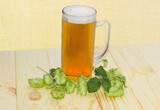 Fototapeta Zwierzęta - Glass mug of beer and hops cones on rustic table