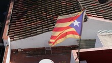 Catalan Flag Flies In The Wind On Sunny Day At The Background Of A Tiled Roof