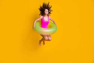 Poster - Photo portrait of young curly girl jumping into pool holding breath closed eyes with inflatable green circle wearing fuchsia swim wear isolated on vivid yellow colored background