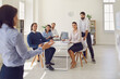 © Studio Romantic - Group of business people in office looking at woman colleague presenting new project or startup idea