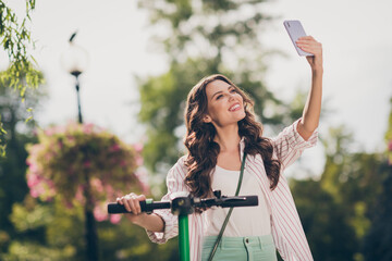 Poster - Photo of nice positive brown curly hair young woman drive segway doing selfie wear striped shirt green jeans enjoy summer fresh air outside