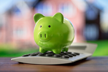 Piggy bank on calculator in front of property, saving to buy a house, real estate or home savings