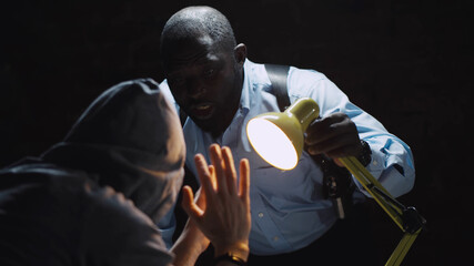 African officer interrogating man suspected of crime glowing light of lamp into face