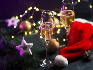 Wall Mural - Festive winter seasonal background, two glasses of champagne on the table with Christmas tree branches, garland, Santa hat