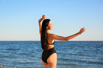 Sticker - Beautiful young woman in black stylish swimsuit on beach