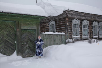 Wall Mural - Russian girl in patchwork coat. Gate, door of wooden house in village near Tomsk city, Russia. Russian folk style in architecture, fashion. Cold season, snow, snowy winter. Seasonal look. Siberia