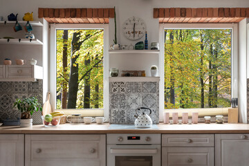 Interior of kitchen with view from window on forest, white wooden furniture and bricks as a decoration. Scandinavian style in a cottage with countertop and plant.