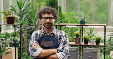 Close up portrait of happy handsome Caucasian businessman standing in apron in own flower shop and smiling to camera. Joyful male florist gardener in green house at work. Small floral store concept