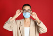 © New Africa - Woman wiping foggy glasses caused by wearing medical mask on red background